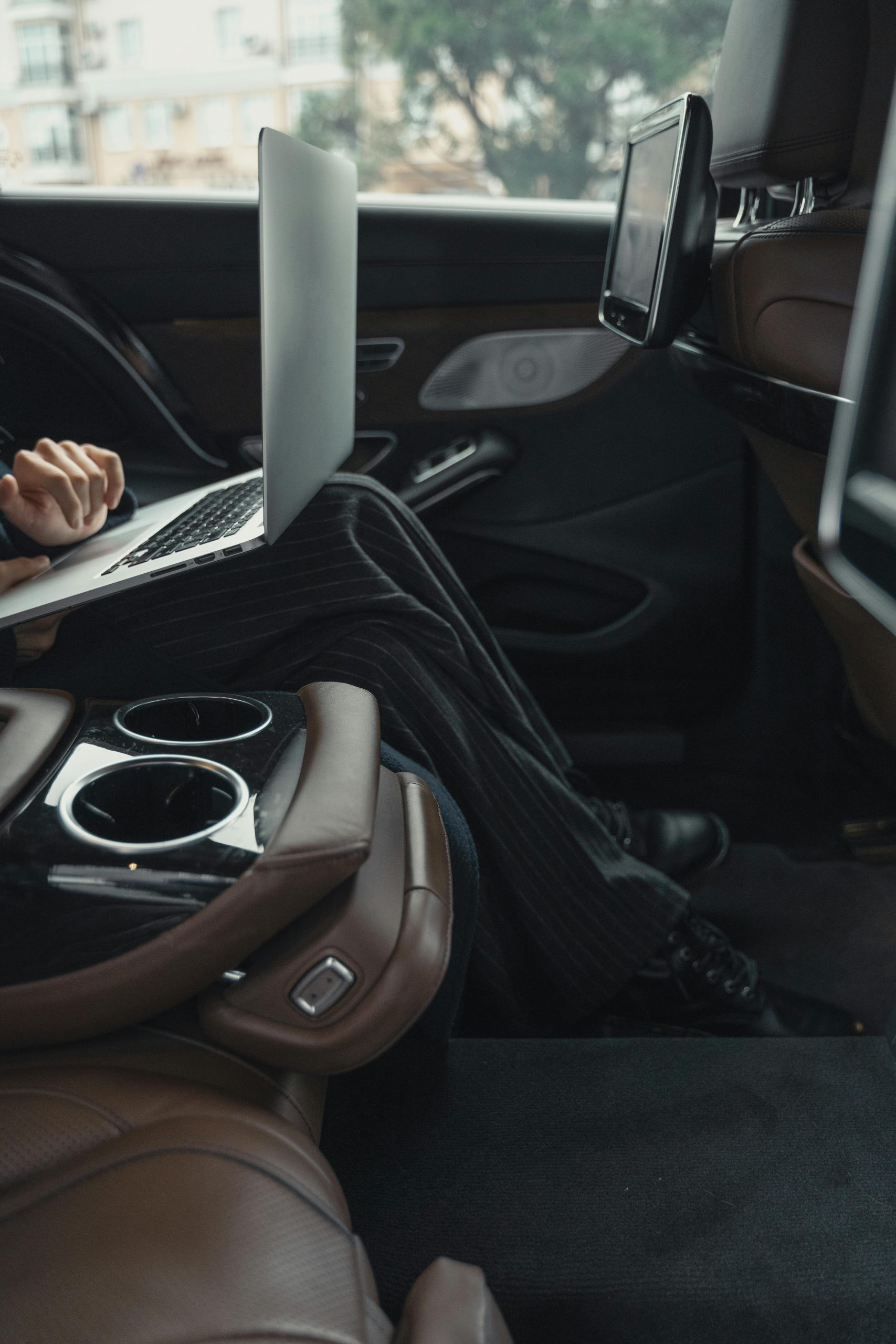 Business passenger using laptop inside luxury car with leather seats and rear entertainment screen